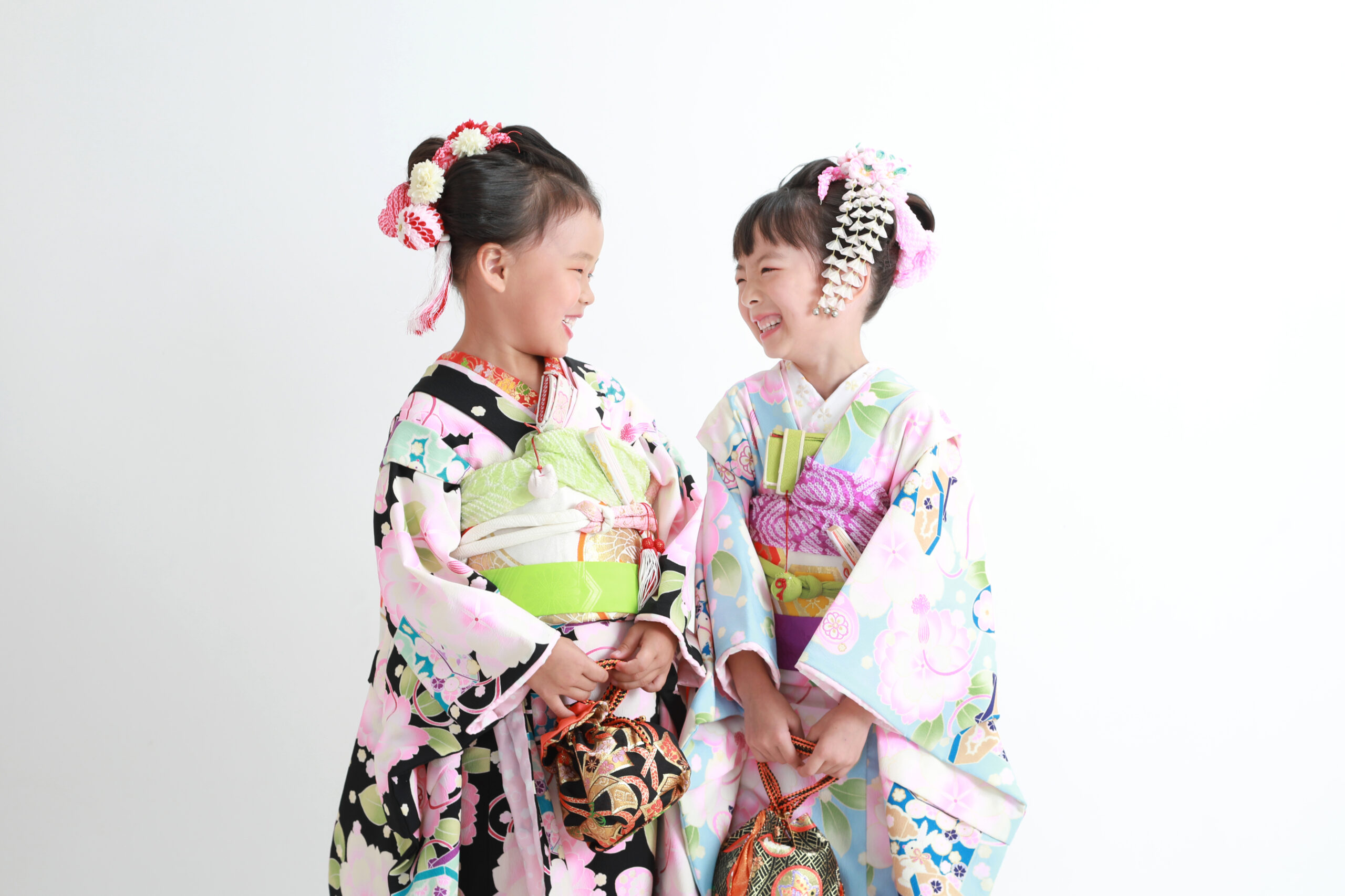 黒の舞妓衣装を着た7歳女の子と水色の舞妓衣装を着た7歳女の子が見つめ合って笑っている写真
