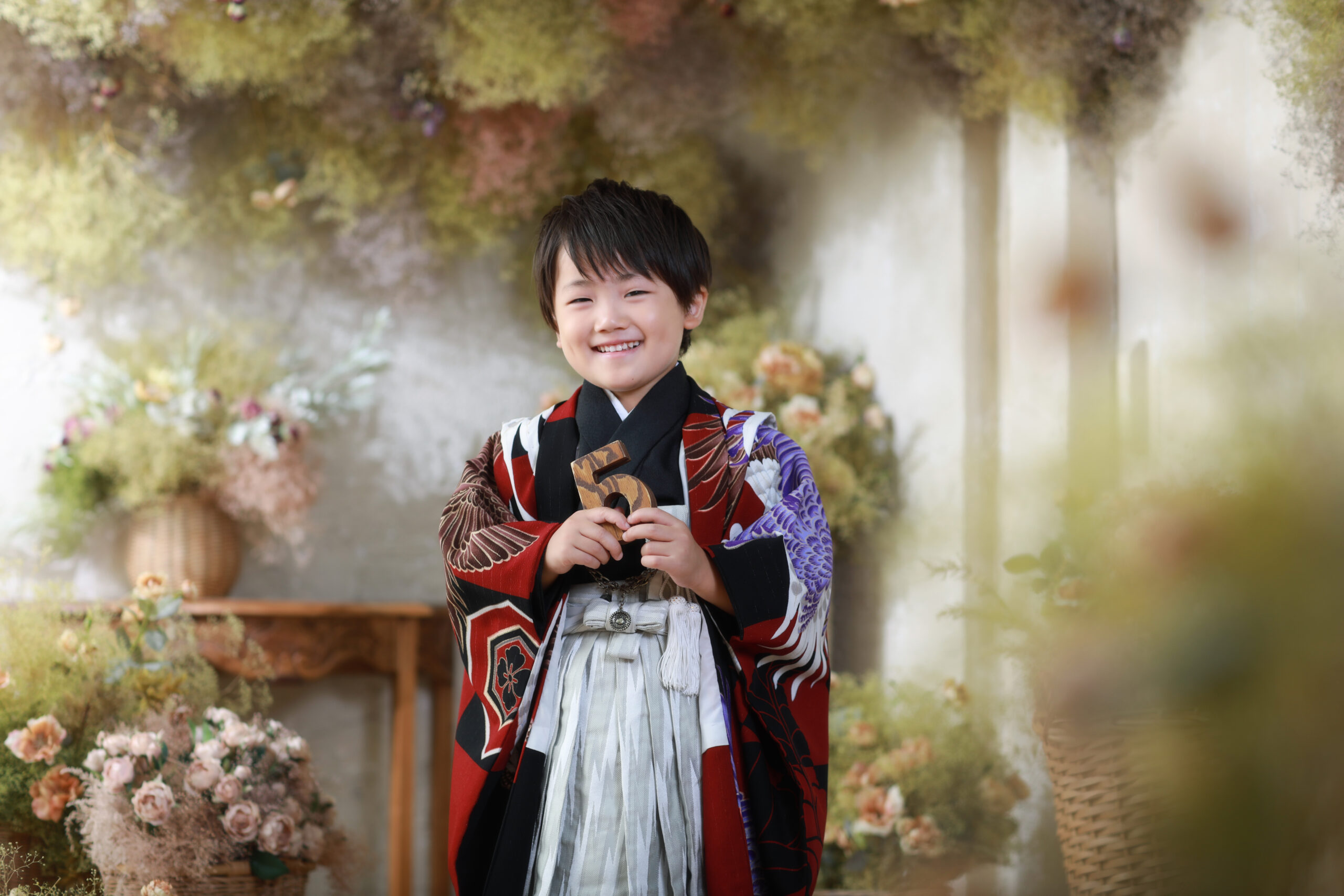 シックな赤い着物を着てドライフラワーのナチュラルなセット背景で撮影した五歳男の子の七五三前撮り写真