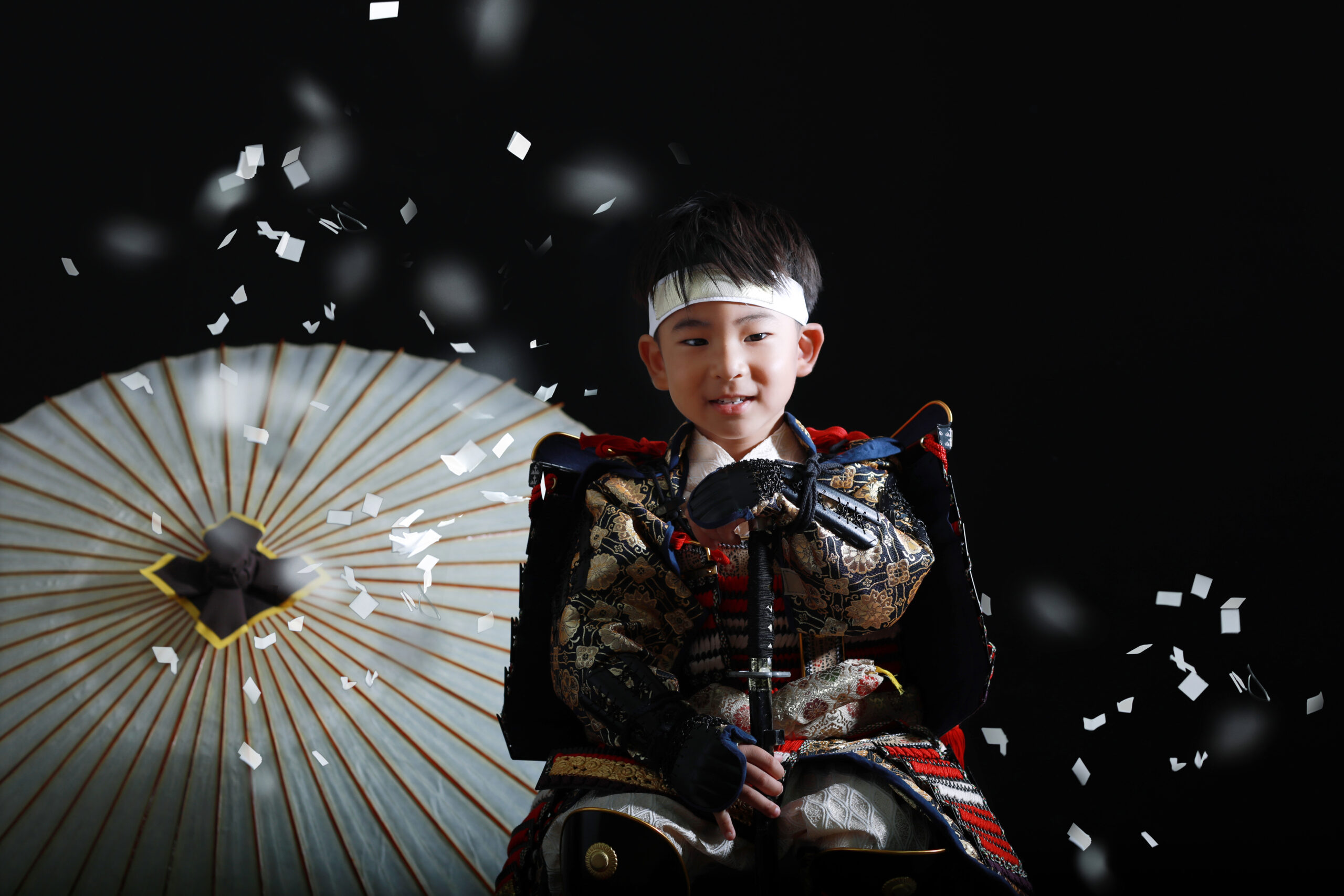 赤い兜を着て紙吹雪の中で佇む五歳男の子の七五三前撮り写真